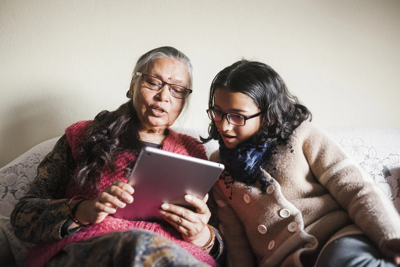 a couple of women sitting on a couch looking at a tablet